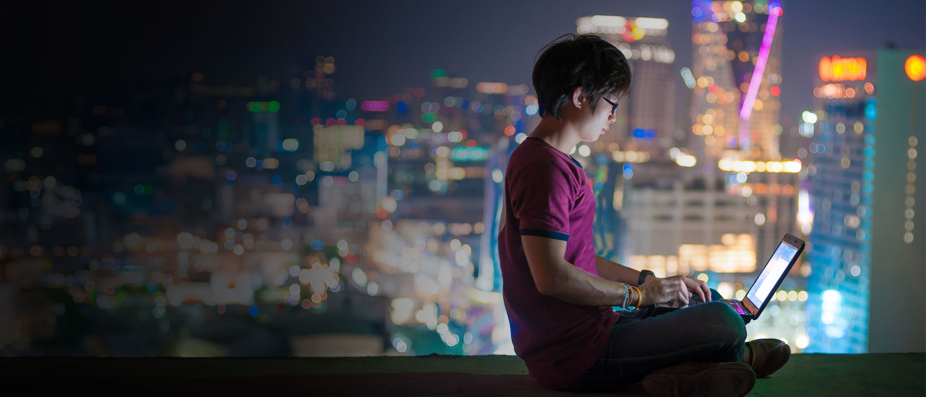 Night time city scape background with person on laptop in foreground
