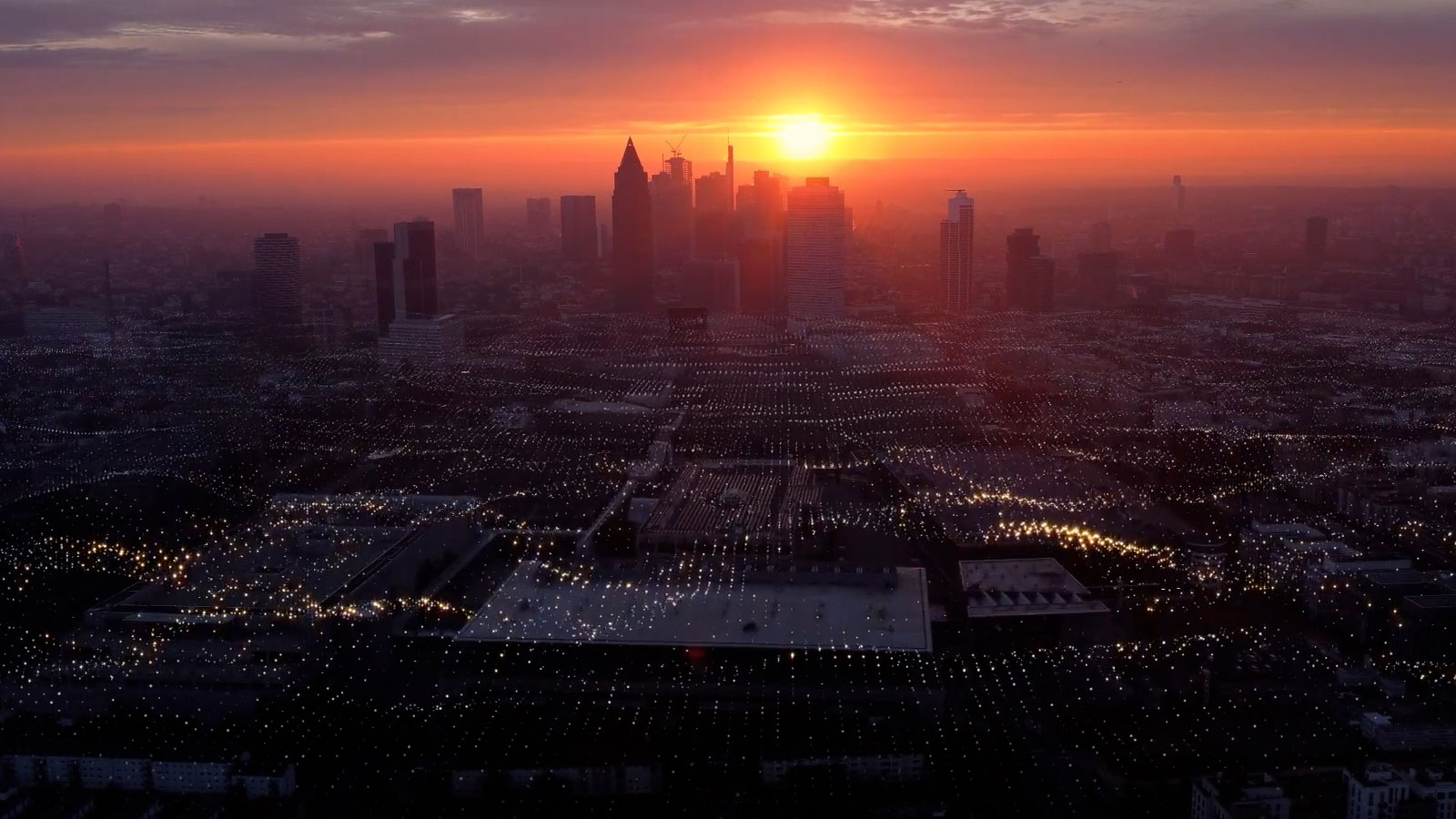 Sunset over a city skyline with a dense network of glowing lights across the foreground