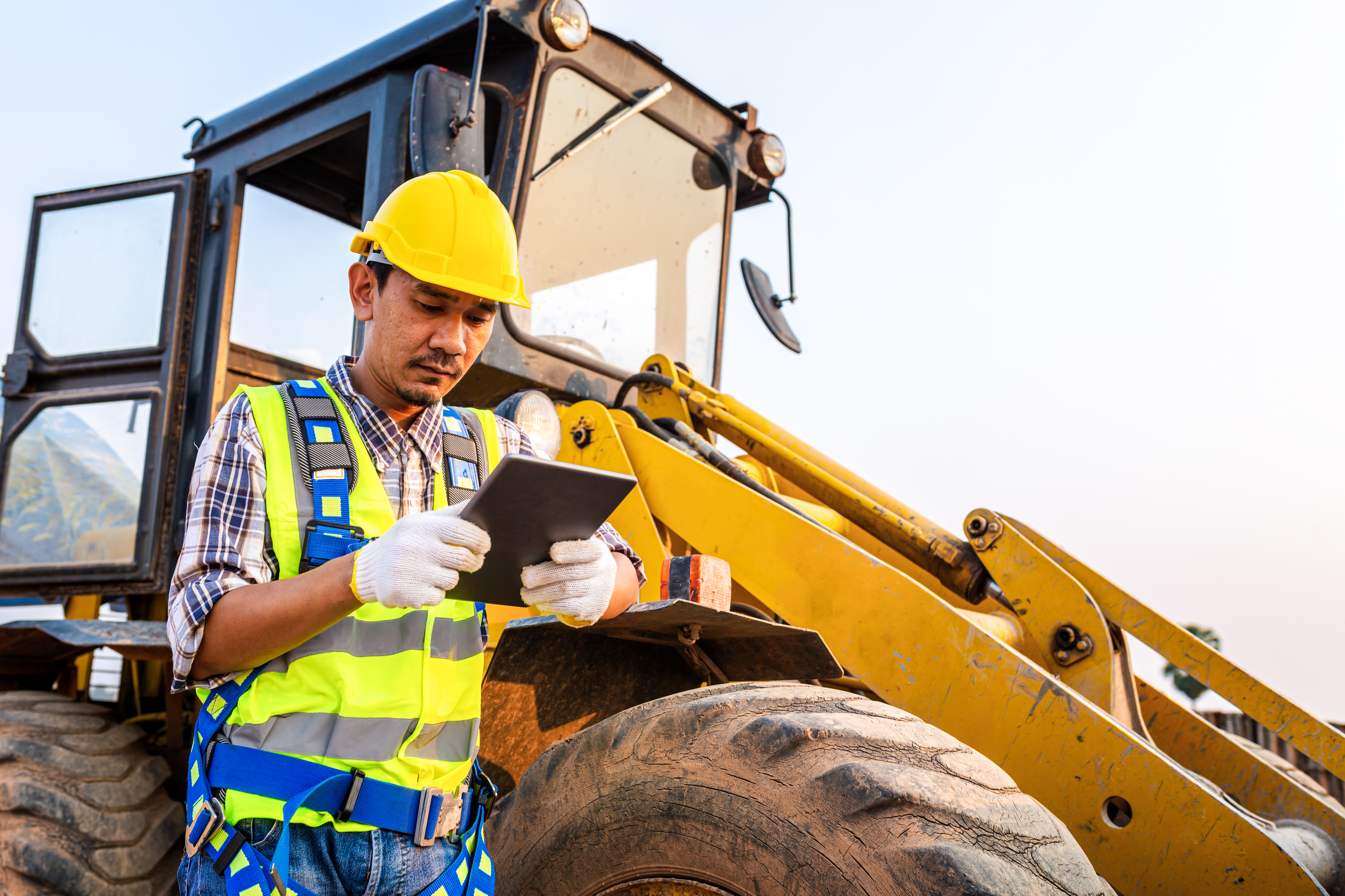 Hard hat worker uses device while leaning against a utility vehicle.