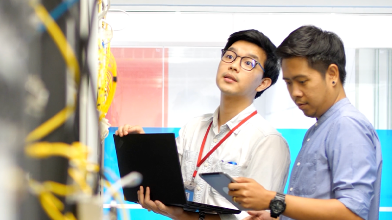 Two workers standing near equipment using a laptop and tablet