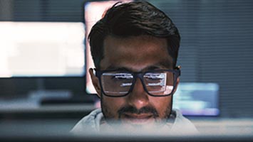 Man in black-framed glasses, with code reflected in his lenses