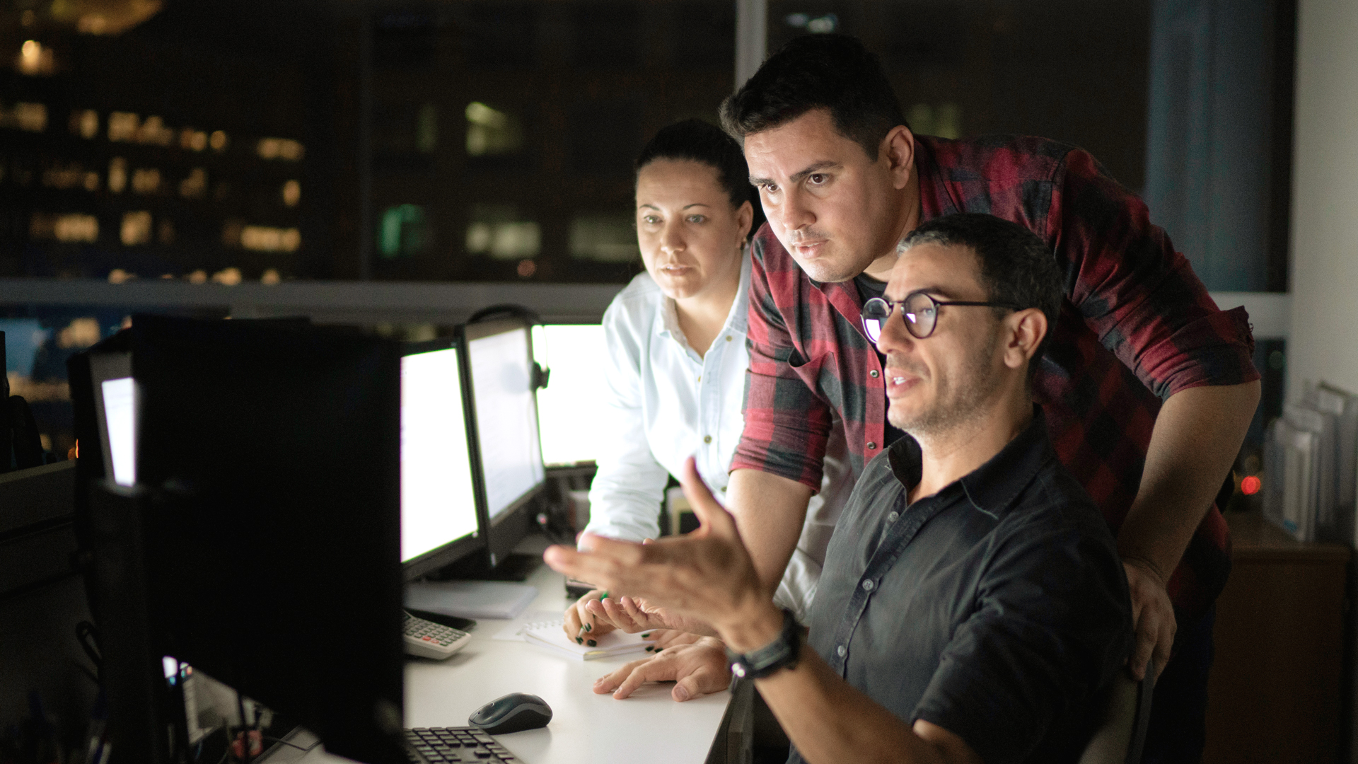 An IT professional at a workstation providing FSO support to two colleagues.