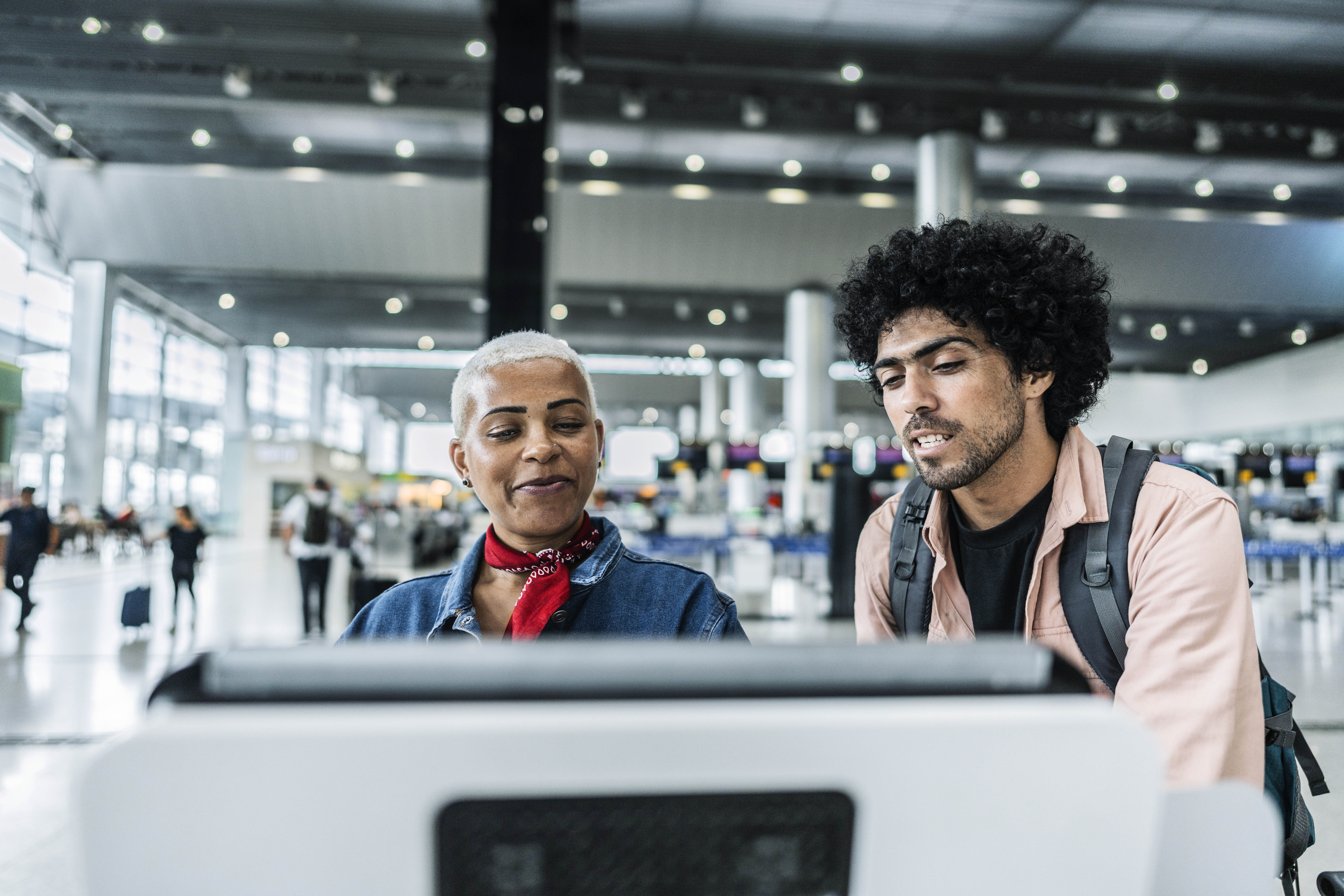 Airport worker helps traveler navigate airport kiosk.