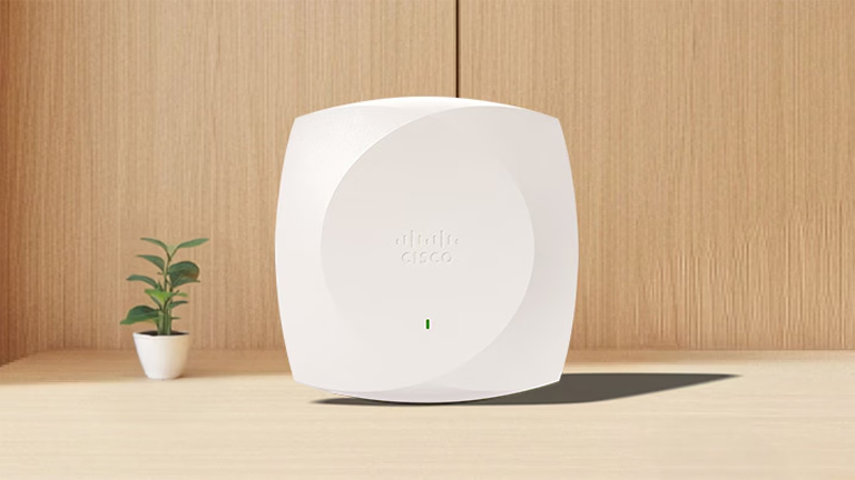 White Cisco wireless access point on a wooden desk next to a small potted plant.